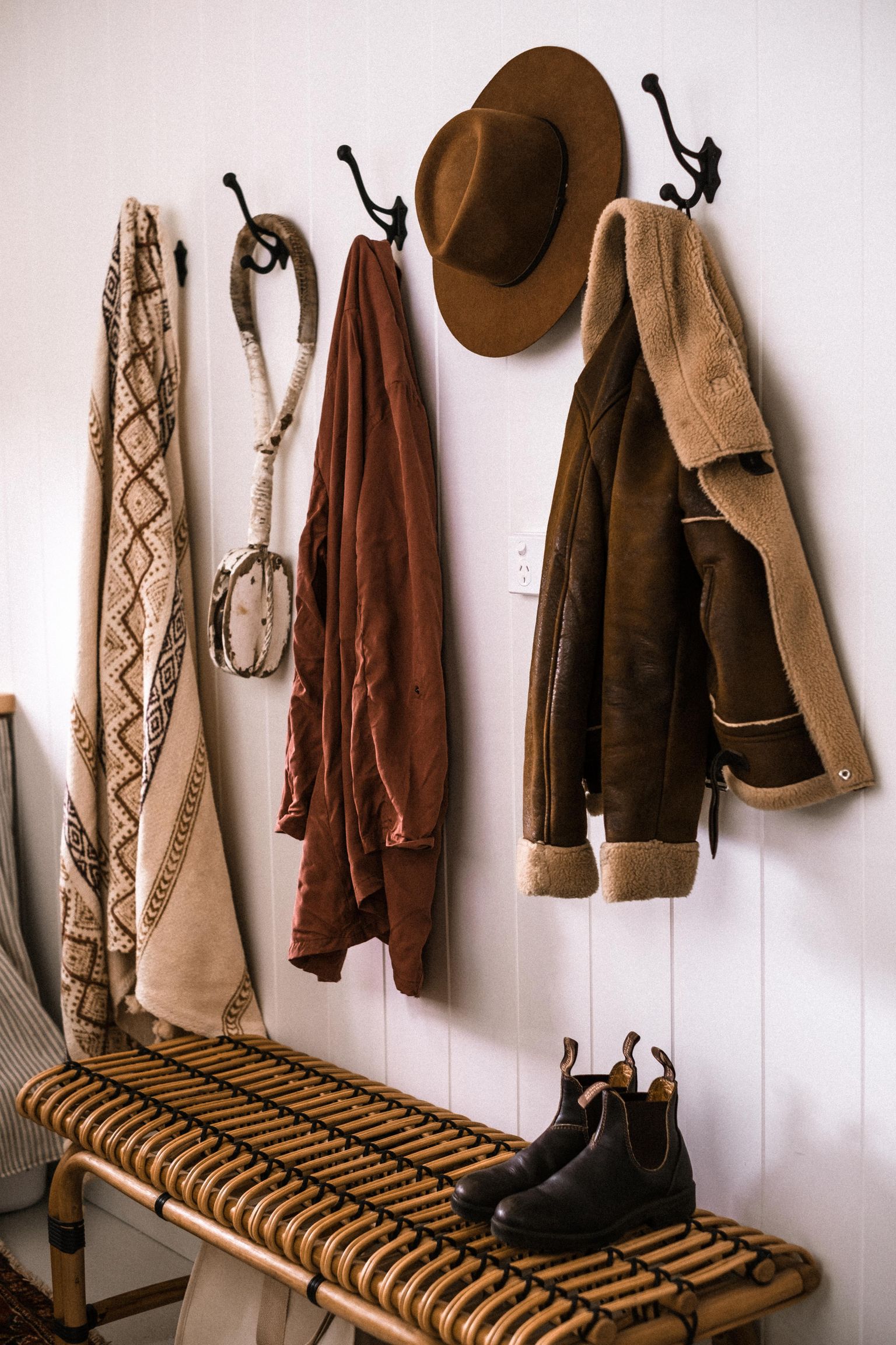 Coats, a hat, boots, and a bench in a real home entryway