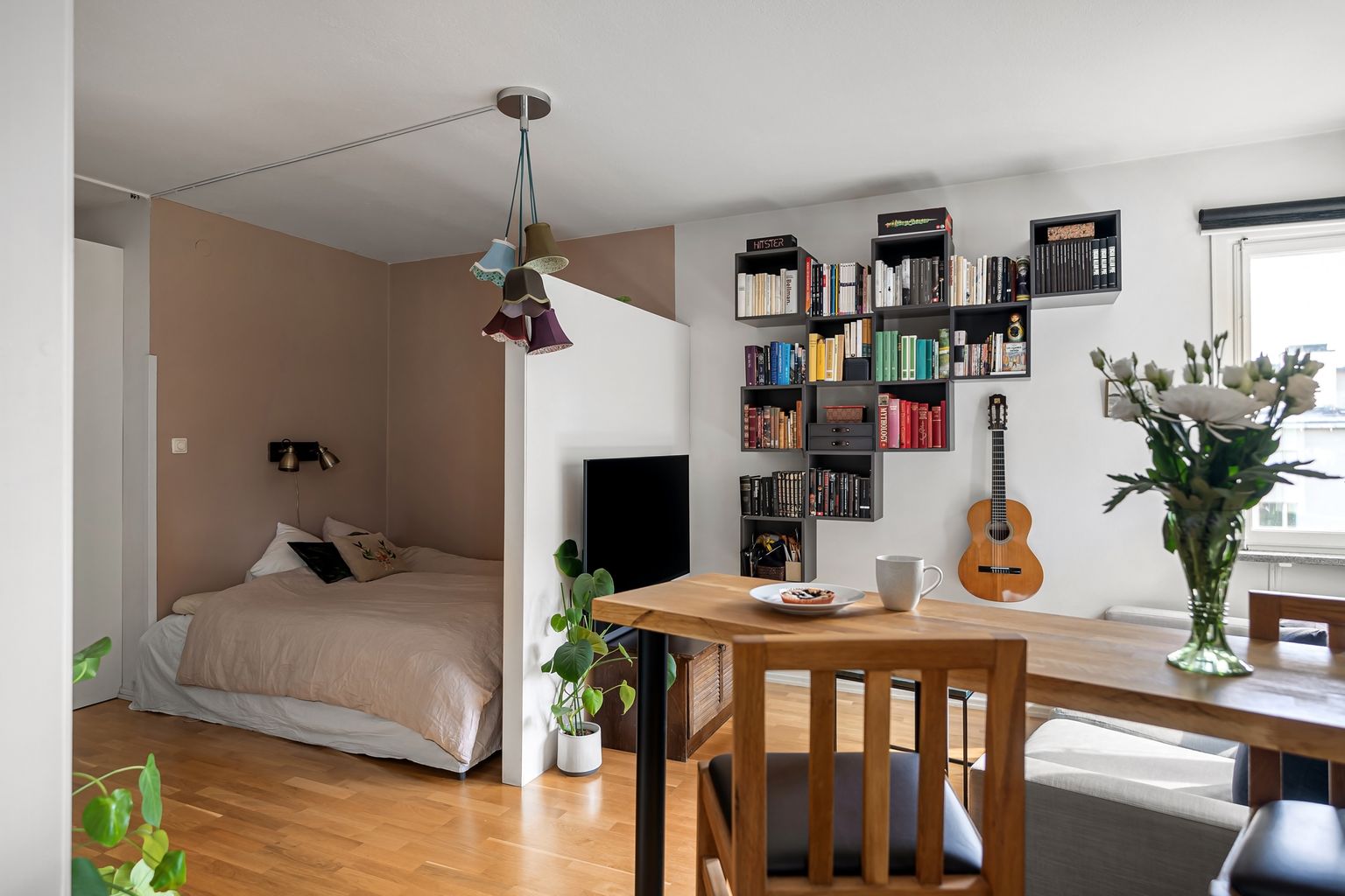A lived-in studio apartment with a bed, dining table, and wall shelving